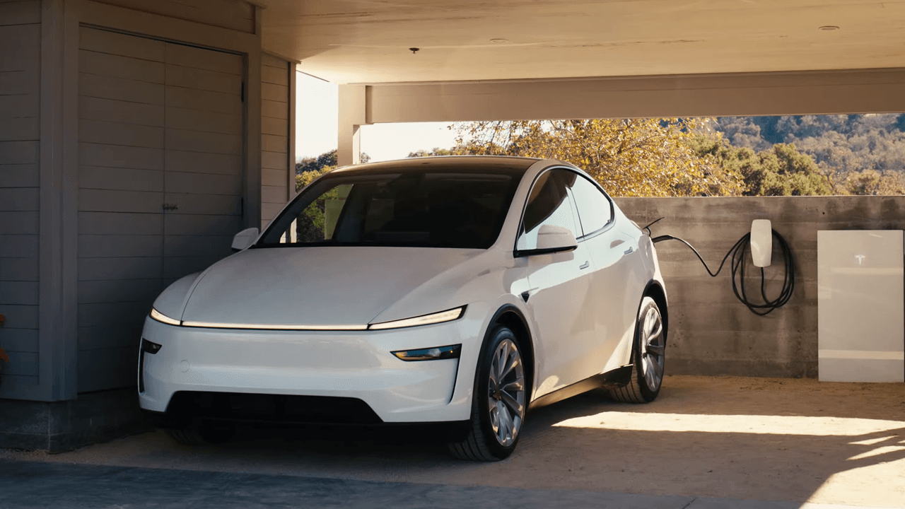 Voiture électrique blanche stationnée sous un abri, en charge avec un chargeur mural situé à droite.