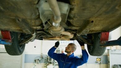 Mécanicien chauve en bleu examinant le dessous d'une voiture levée. Vue de l'échappement et des pneus.