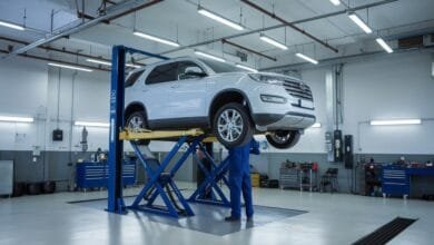 Mécanicien en bleu travaillant sous un SUV blanc d'occasion surélevé sur un pont élévateur dans un garage moderne lumineux