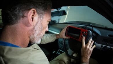 Un homme à barbe grise utilise un scanner OBD rouge pour diagnostiquer une voiture.